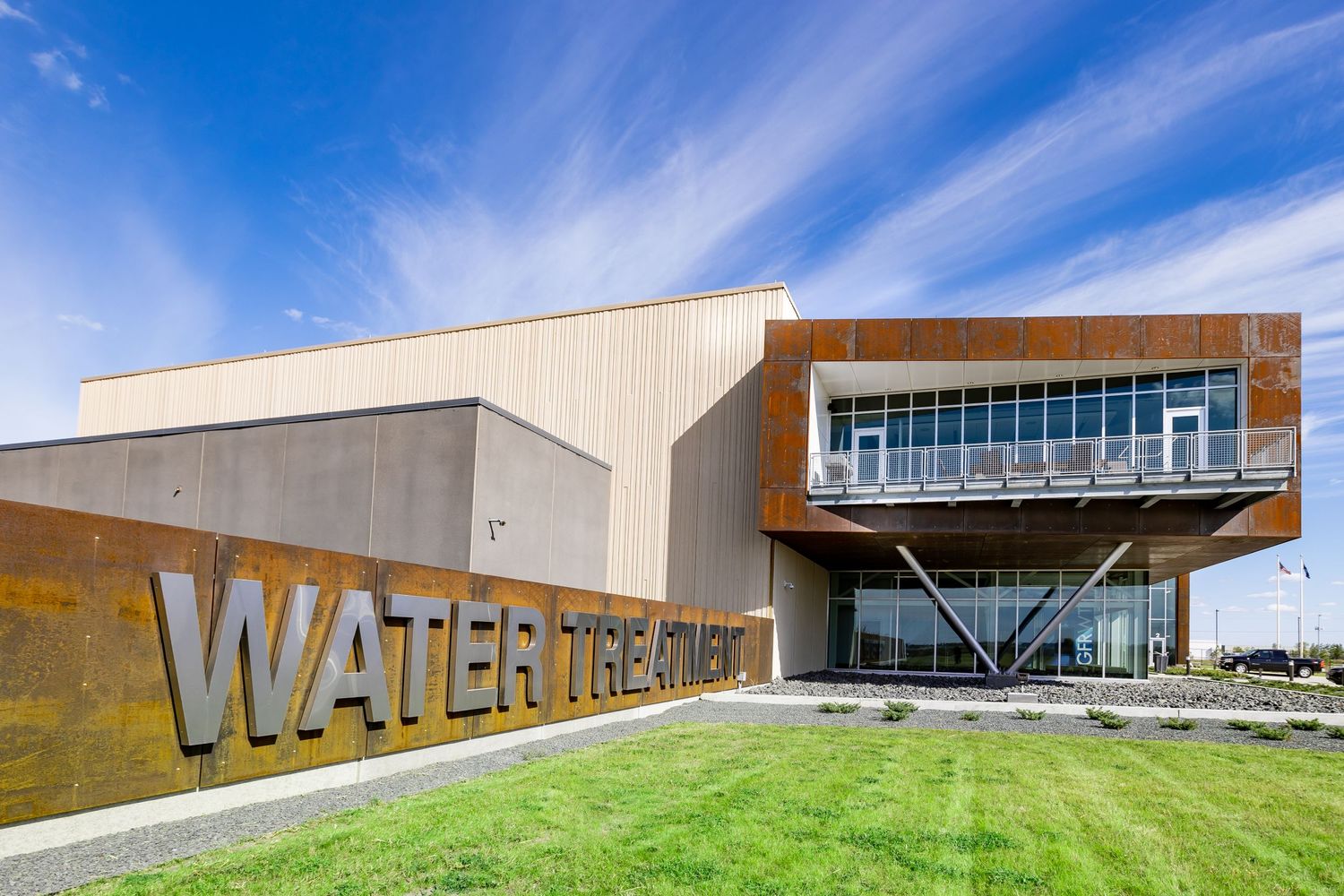Long modern building with glass facade under bright blue sky with wispy clouds.