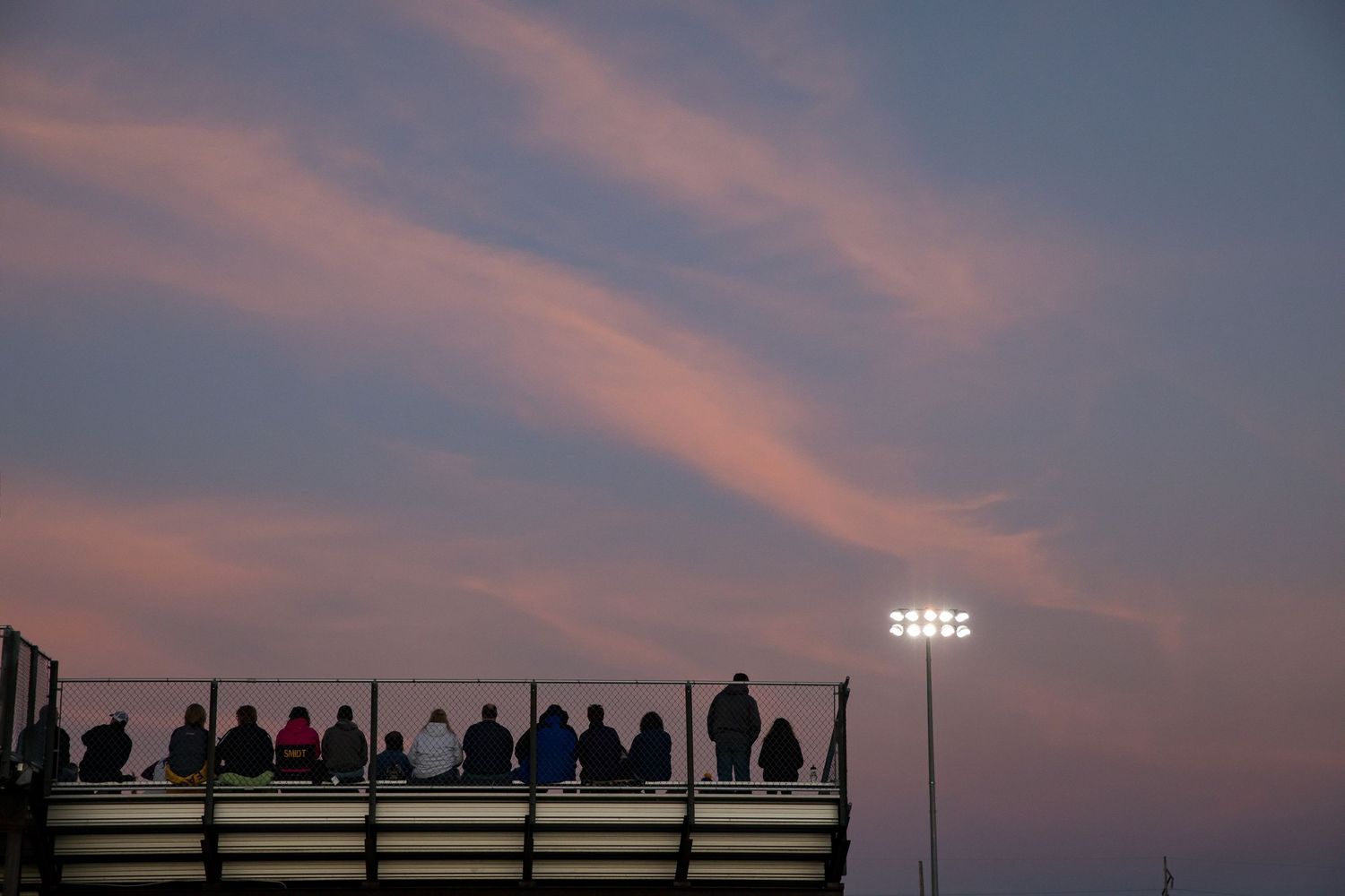 Silhouettes of spectators watching sunset against stadium lights.