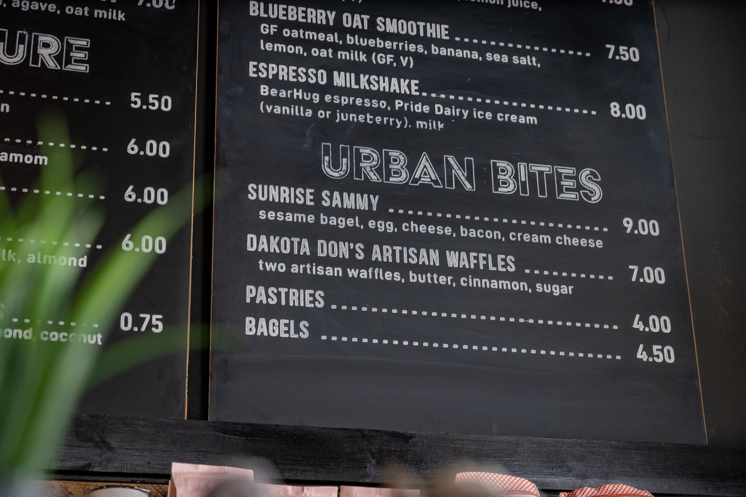 Menu board displaying urban cafe offerings and prices written in white chalk on a dark background.