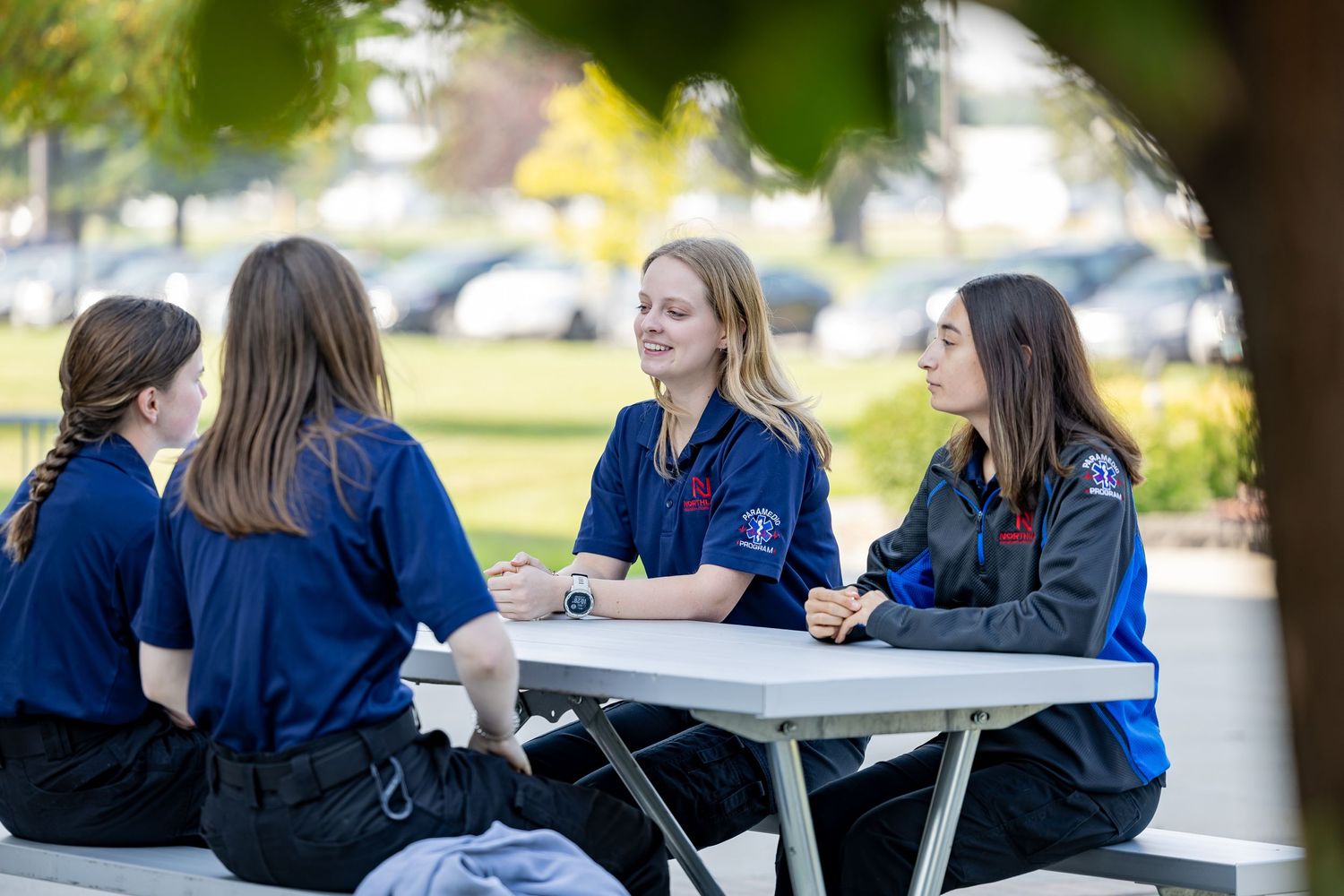 Students in blue uniforms having a discussion at a white outdoor table.