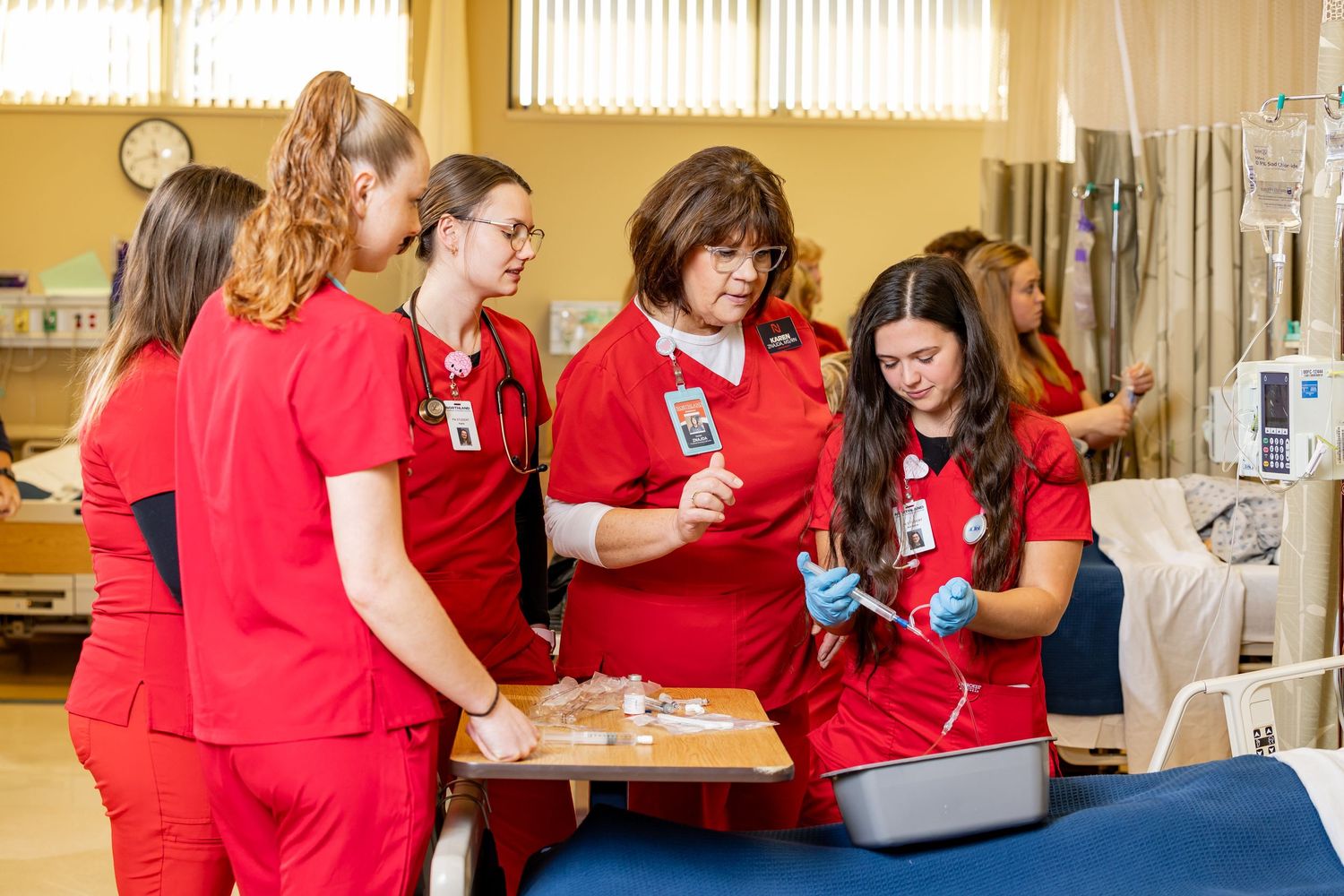 Healthcare workers in red scrubs reviewing medical information in a hospital room.