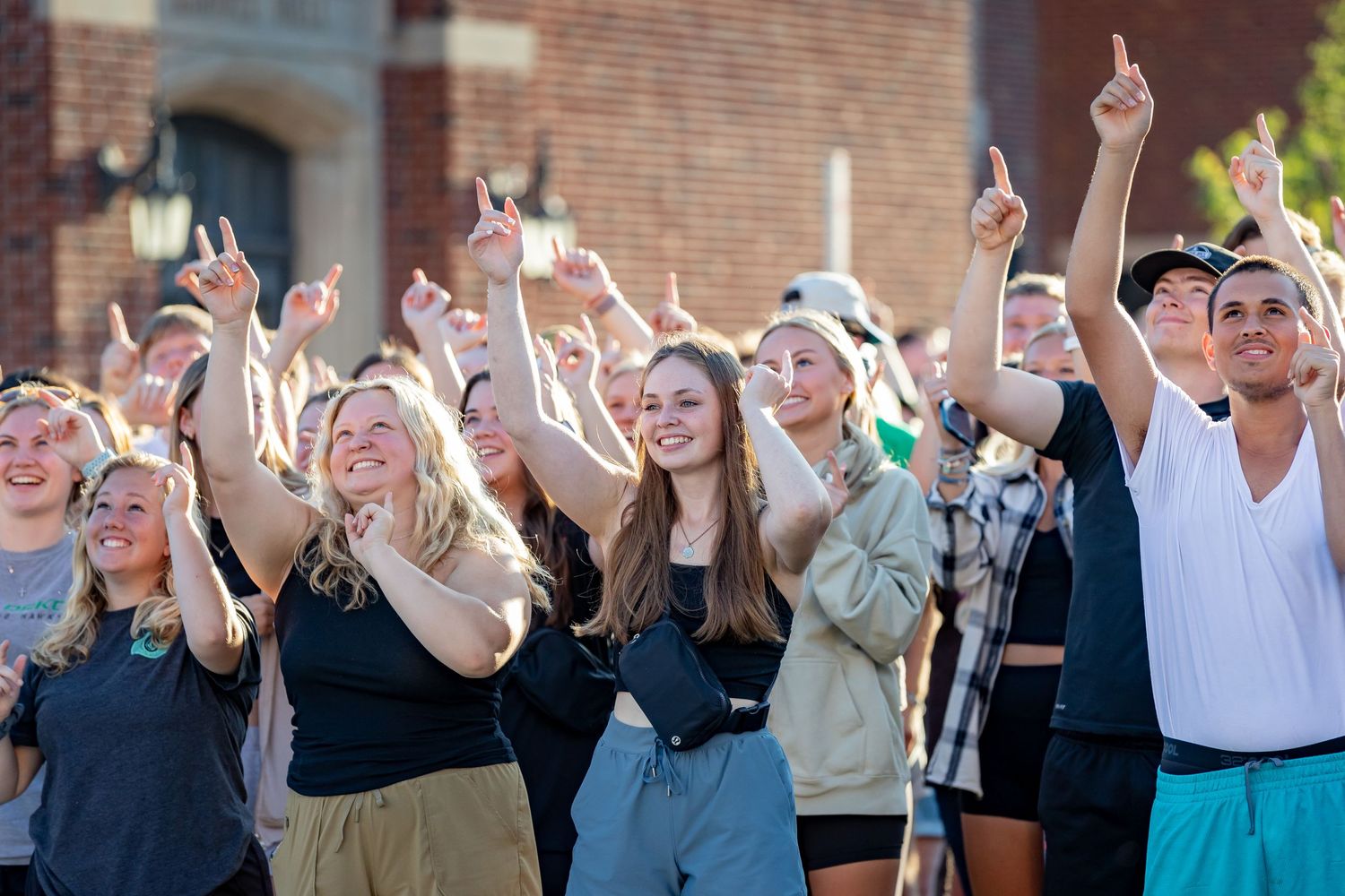 Large crowd of students celebrating outdoors with raised arms and excited expressions.