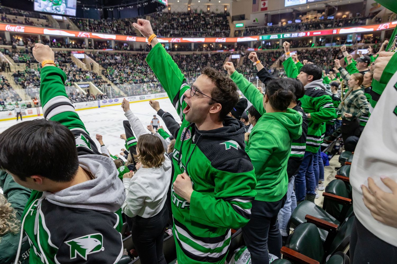 Sports fans in green jerseys celebrating enthusiastically at stadium event.