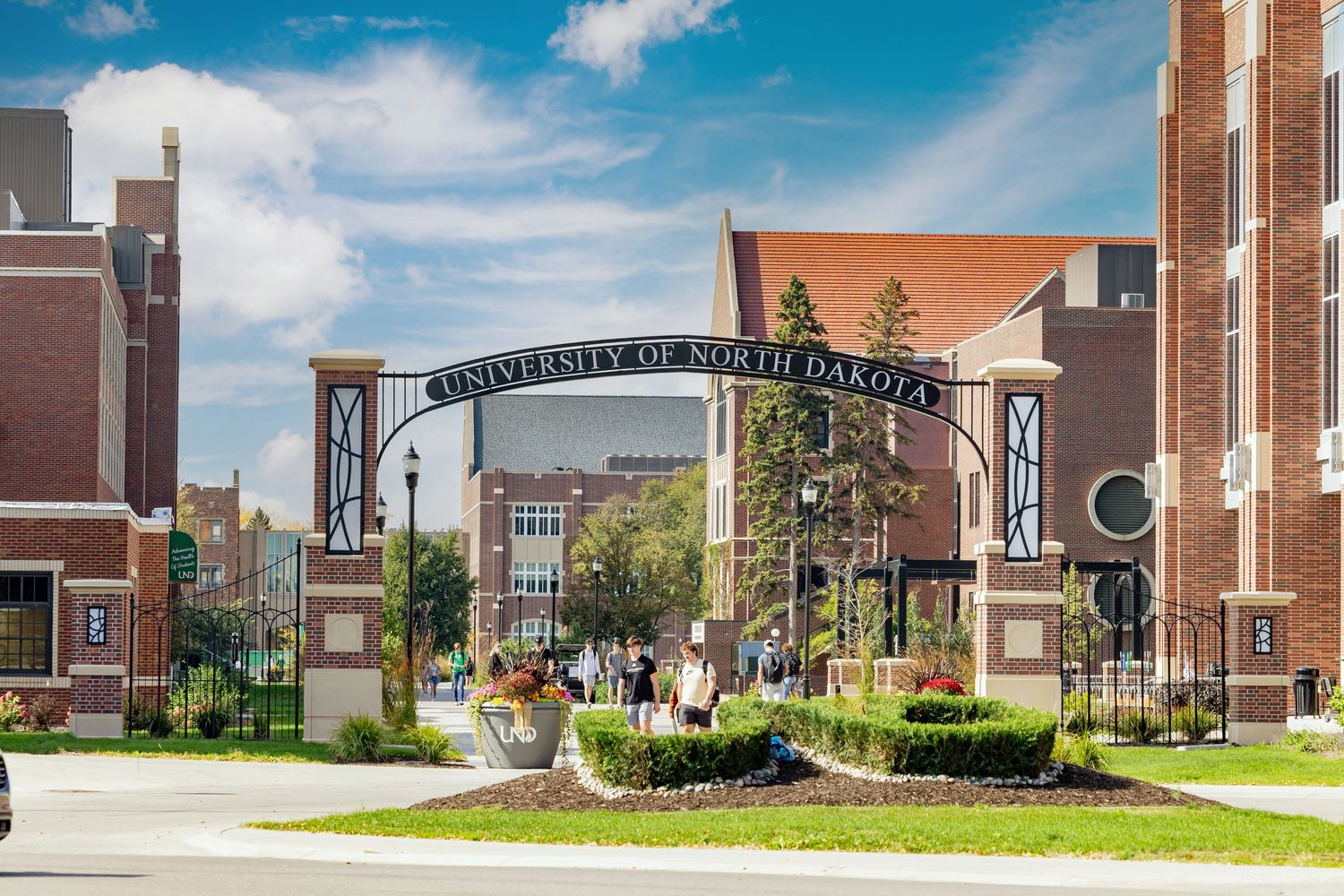 Wide panoramic view of a university campus with brick buildings under a bright blue sky.