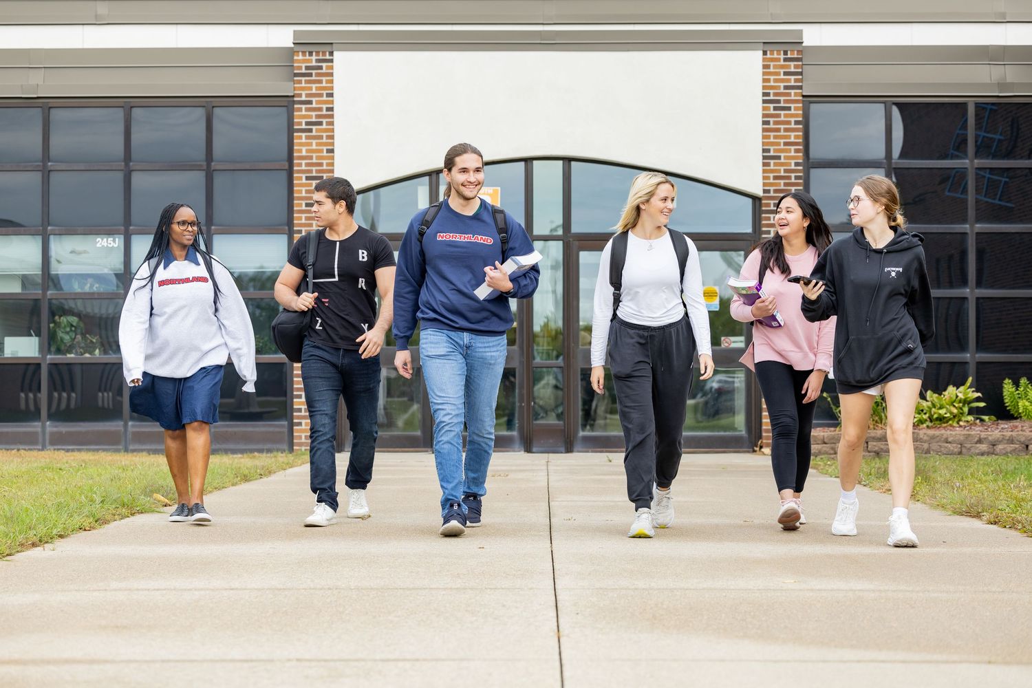 Students walking along sidewalk outside brick school building.