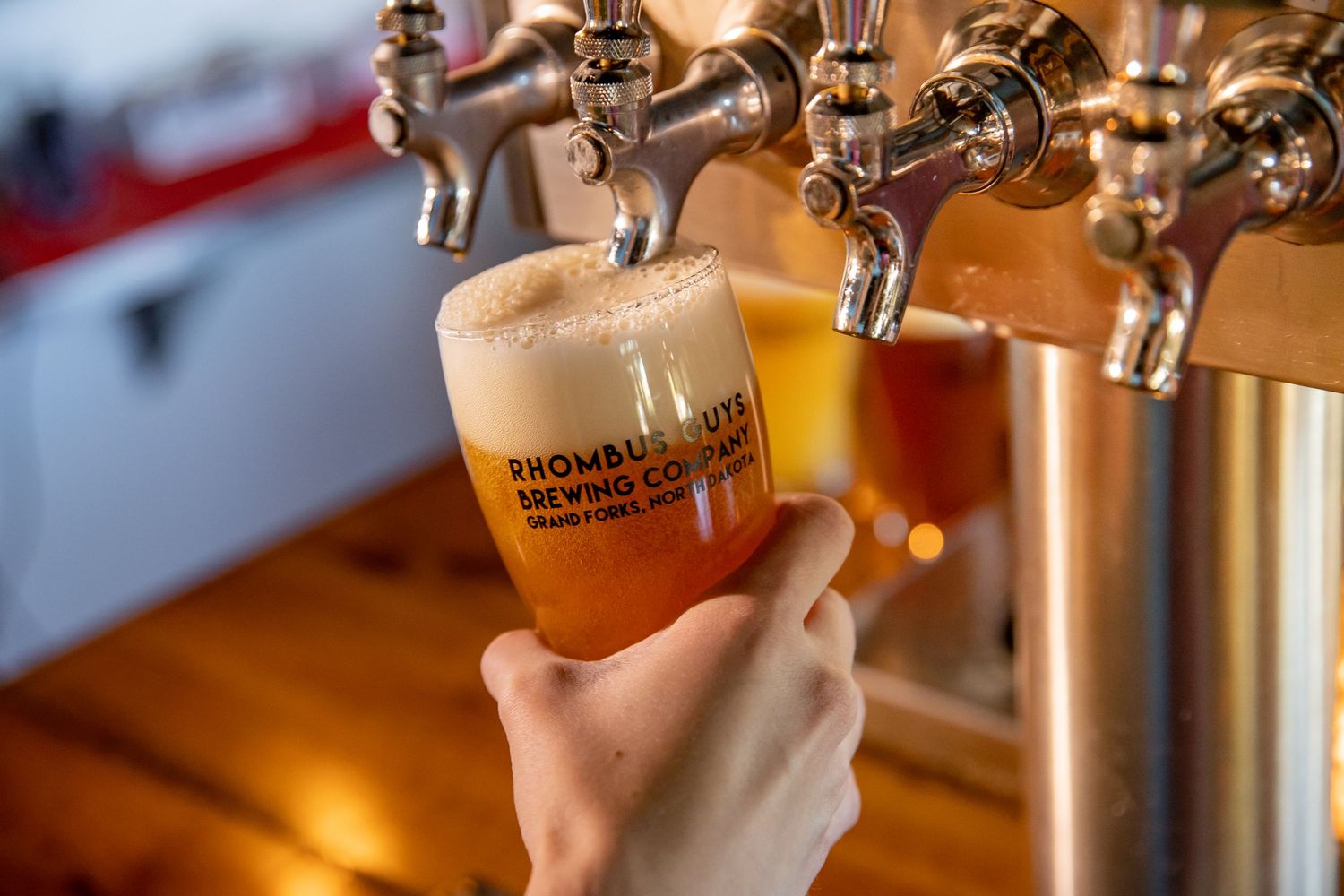Beer taps at bar with warm lighting and glasses being filled.