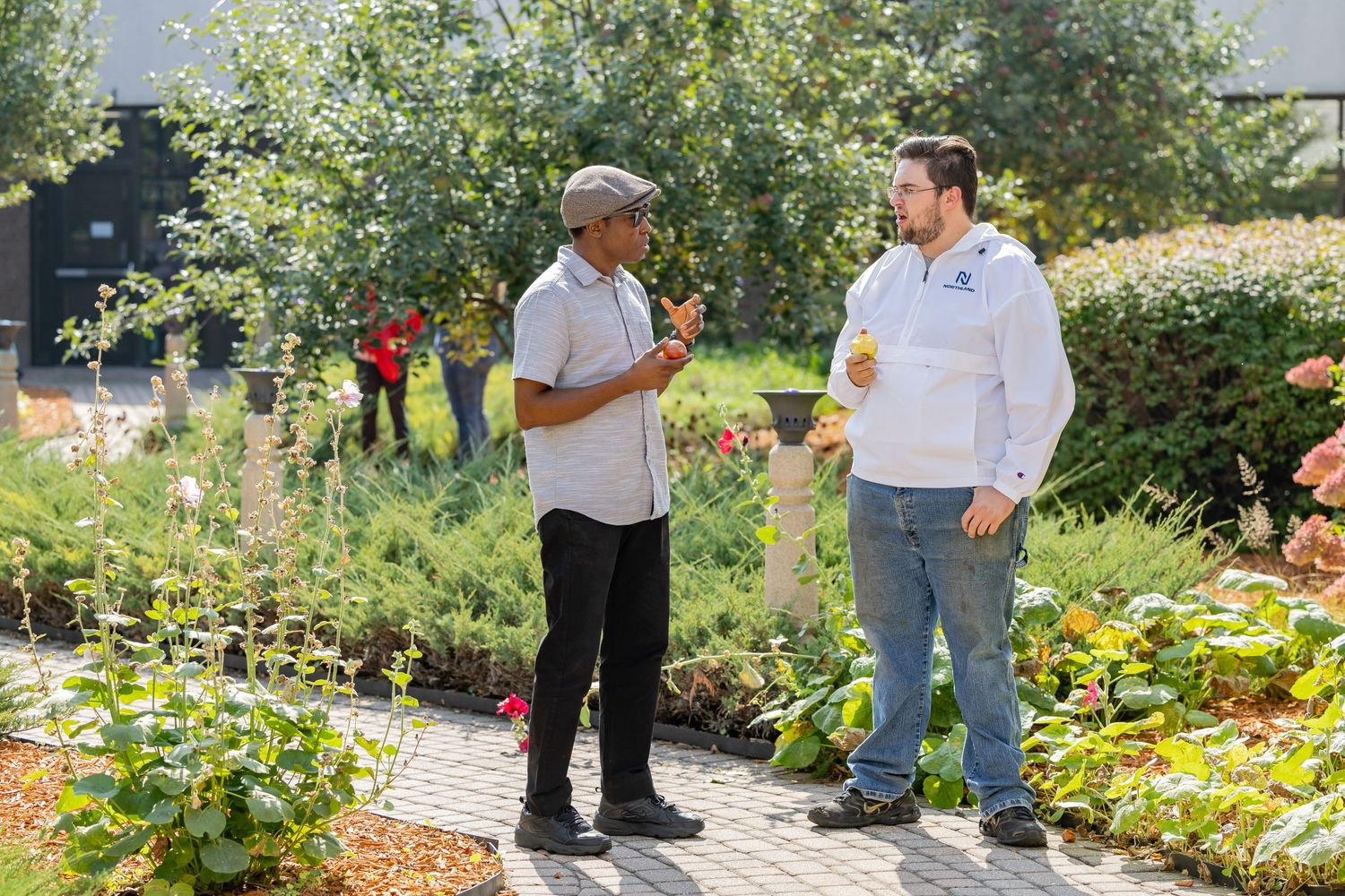 Two people having a conversation in a colorful garden setting on a sunny day.