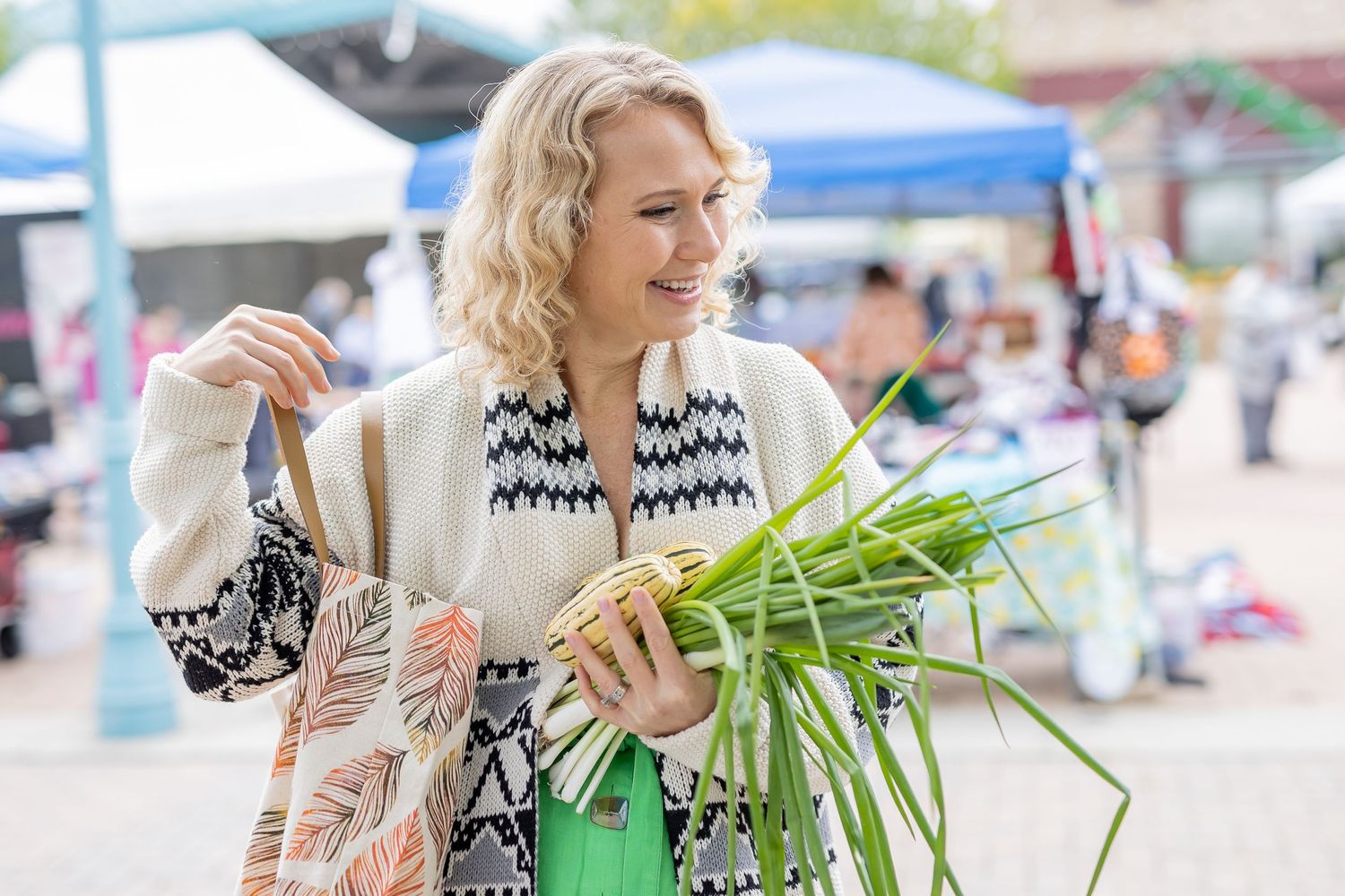 Shoppers browsing at an outdoor farmers market with fresh produce and vendor stalls.