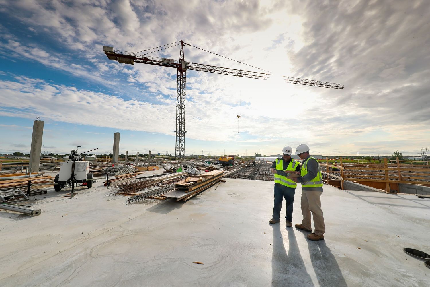 Construction site workers reviewing plans on a sunny day with cranes in background.