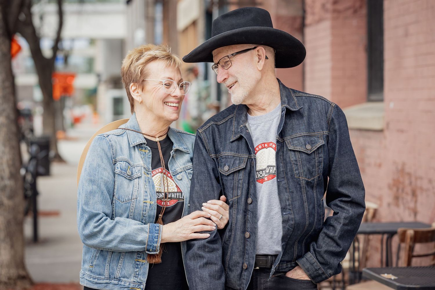 Couple sharing a moment together on an urban sidewalk wearing denim and western attire.