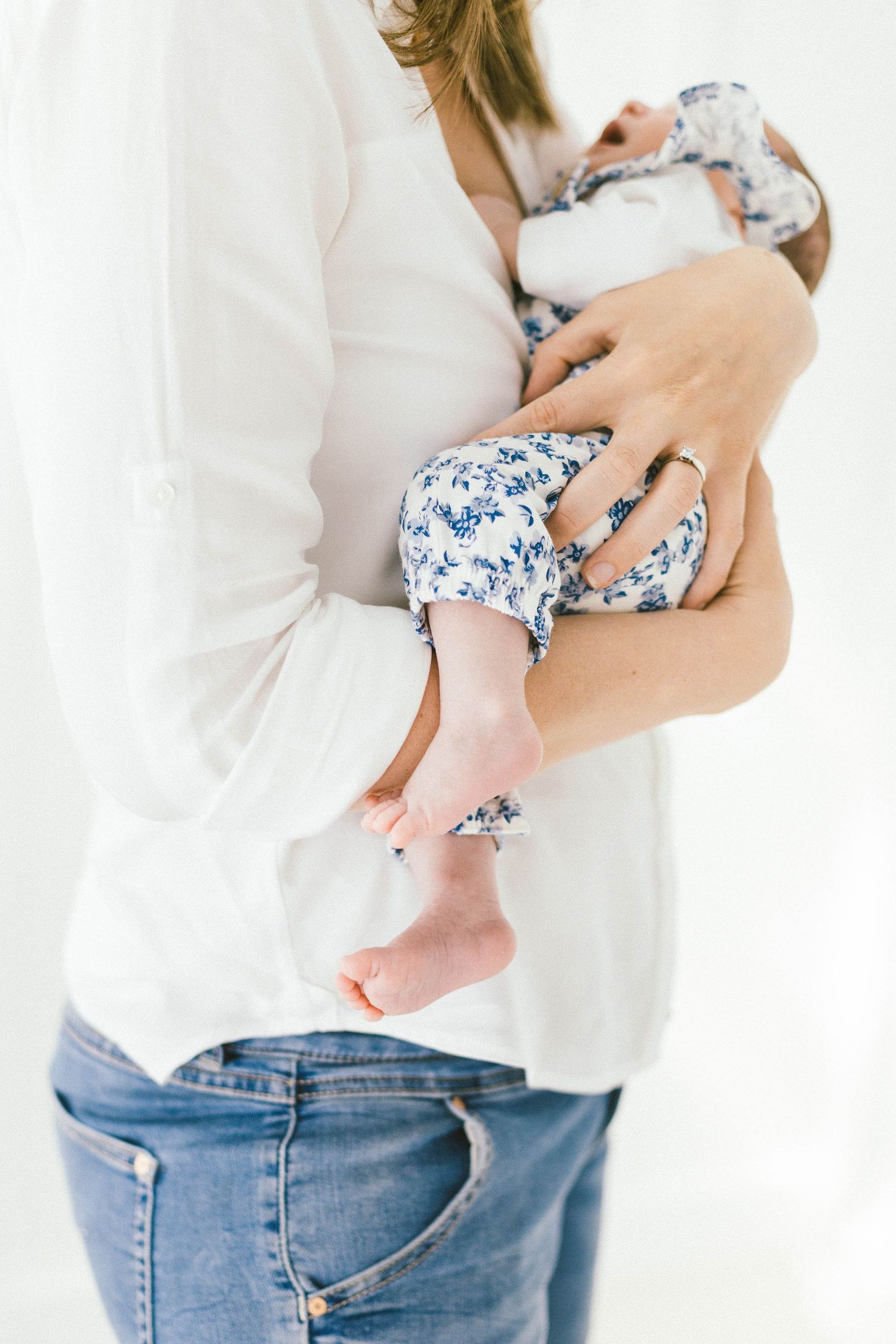 Parent holding baby wearing blue floral outfit against white background.