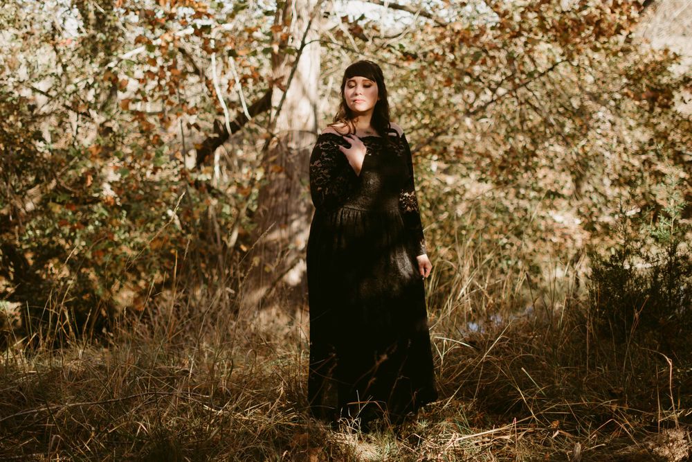 A moody forest portrait featuring someone in a flowing black lace gown against autumn foliage.