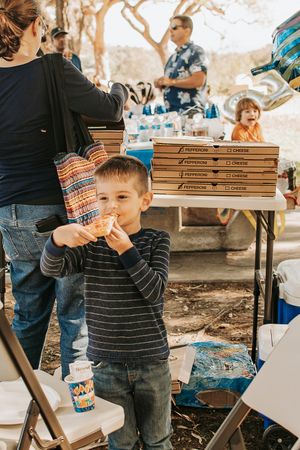 Children at an outdoor party preparing to eat slices of pizza from stacked delivery boxes.