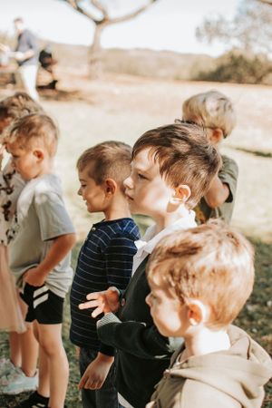 Children lined up outdoors watching something with excited expressions on their faces.
