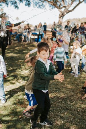 Children playing with bubbles during an outdoor party under shady trees.