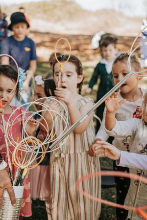Children blowing party favors while standing together at an outdoor celebration.