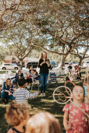 Group gathers under shady trees at an outdoor community event with bubbles and activities.