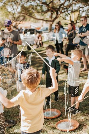 People waving bubble wands in the air at an outdoor party under trees.
