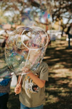 Giant soap bubble floating in a sunlit outdoor park setting.