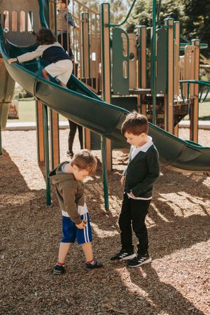 Two children playing near a green playground slide in a park.