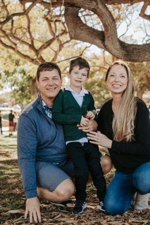 A heartwarming family moment captured under a large tree in a park setting.