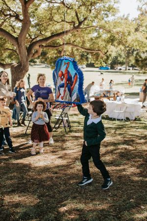 Kids running and playing with bright blue pinatas at a park celebration.