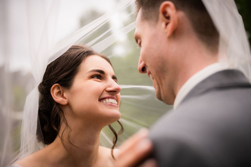 Bride and groom under veil laughing close up