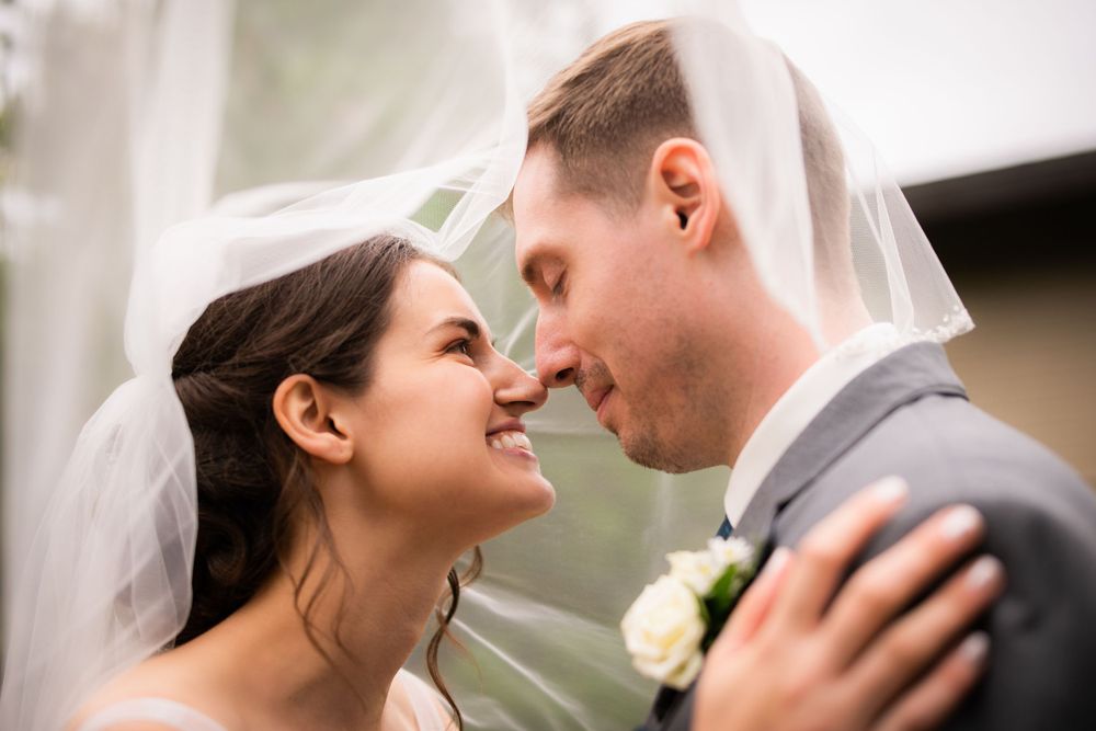 Bride and groom under veil laughing close up