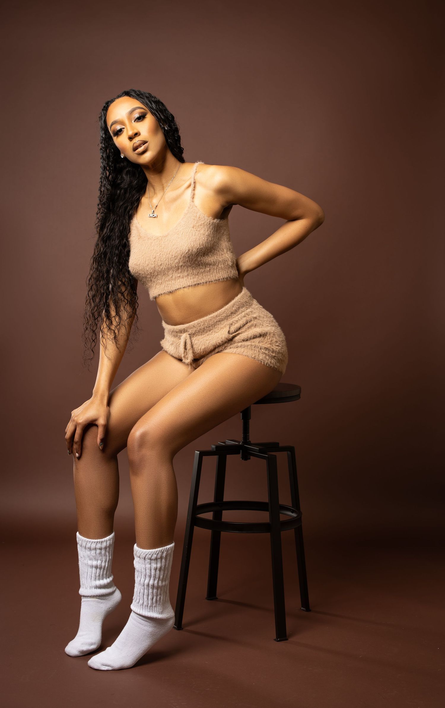 Fashion portrait in beige knit set and white socks on dark stool.