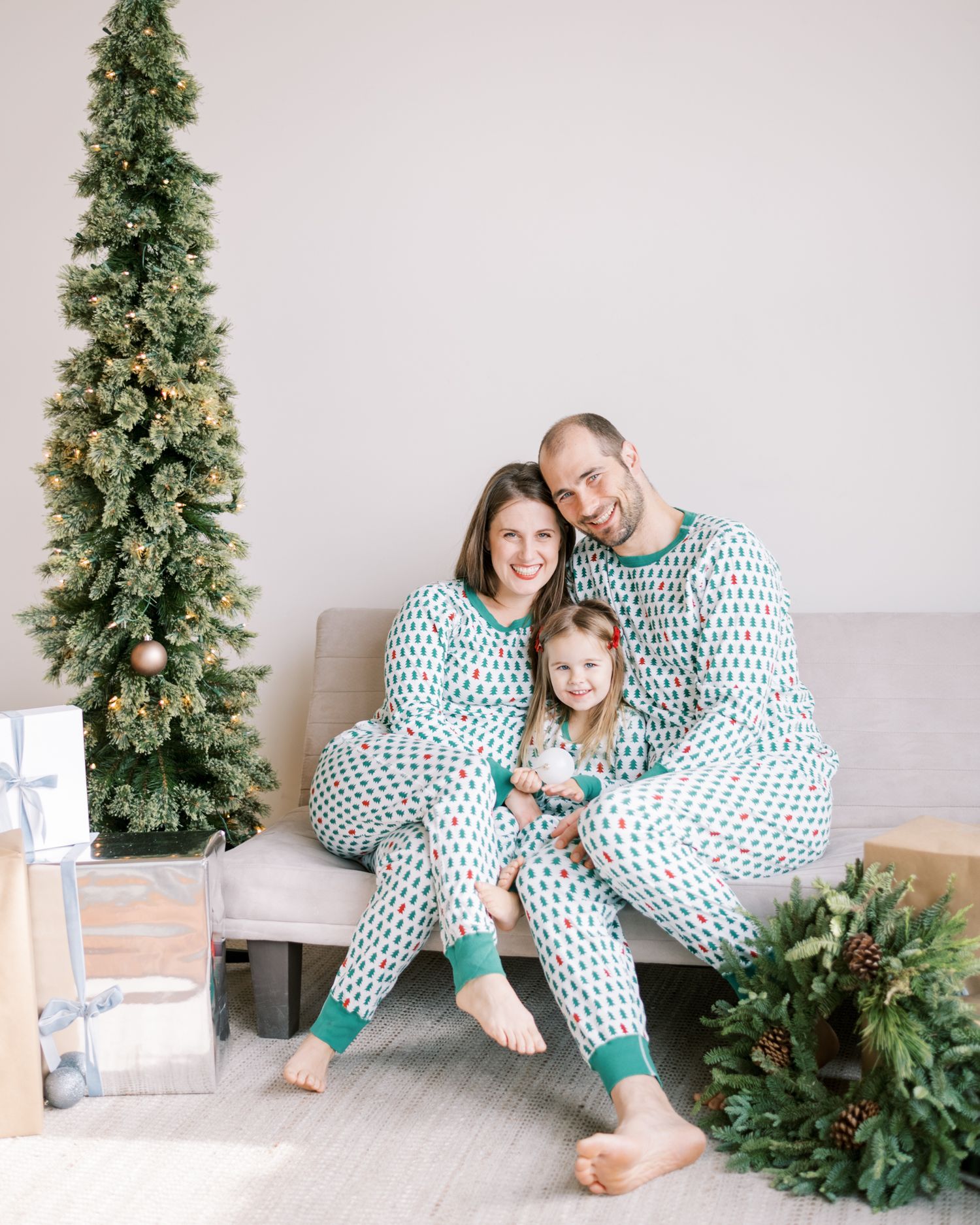 Family wearing matching geometric pattern pajamas posing by Christmas tree.