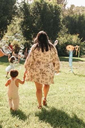Two people walking on grass near bubble stations and party decorations in sunlit garden.