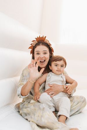 Joyful indoor portrait with decorative lion headpiece against white background and balloons.
