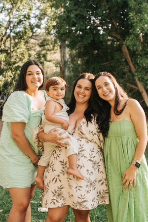 Group photo outdoors with people wearing green and floral dresses against natural backdrop.