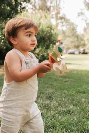 A toddler in beige overalls playing with toys in a sunny garden setting.
