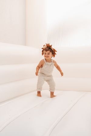 Energetic toddler wearing leaf crown jumps and plays on white backdrop.