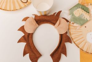 Brown lion-themed headband accessory with ears displayed on white surface.
