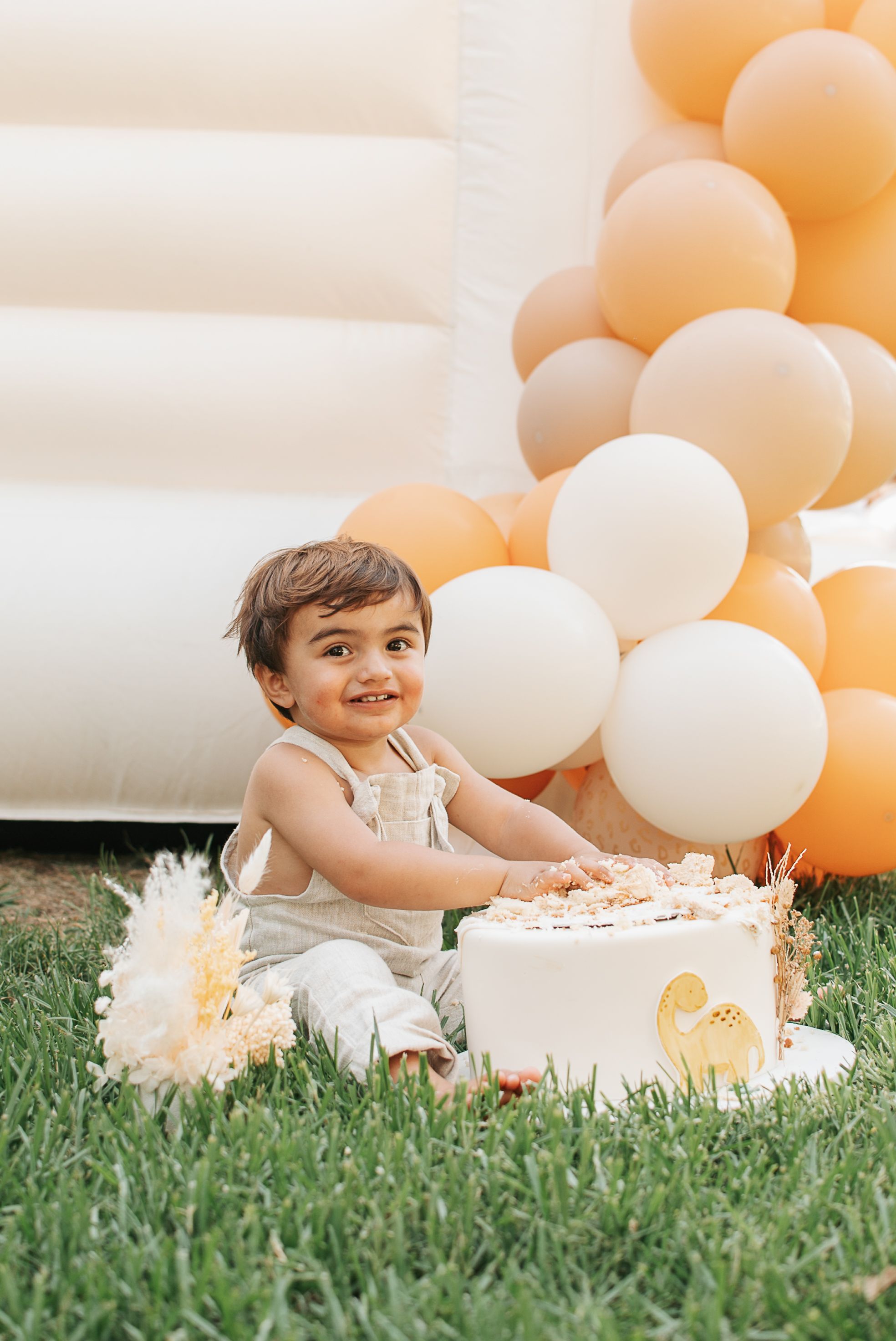 Outdoor party setup with peach balloons, white cake, and decorative elements on grass.