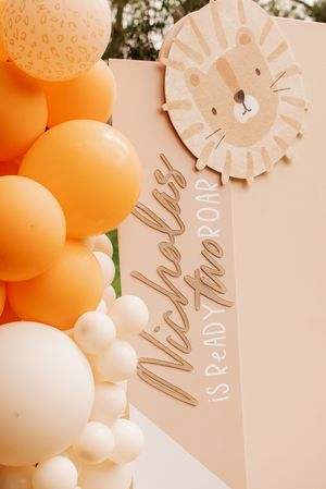 Orange and white balloon arch with lion-themed party sign.