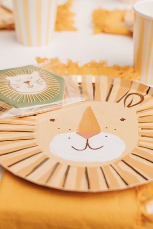 Close-up of lion-themed party plate with cute cartoon face design on orange table runner.