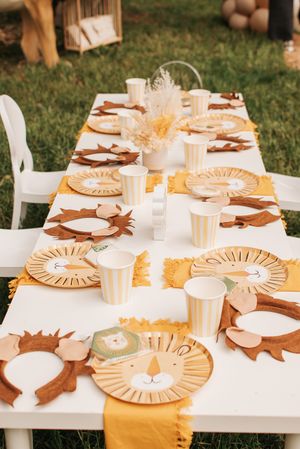 Lion-themed party table with decorative plates and orange accents on white tablecloth.