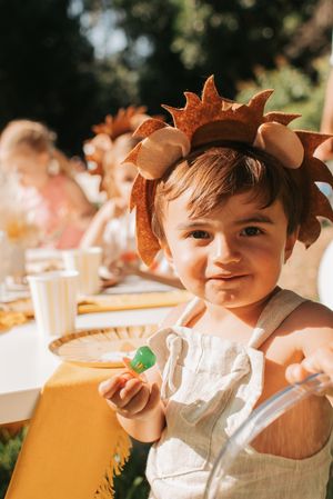 Sweet autumn-themed photoshoot featuring a toddler wearing fall leaf decorations and white overalls.