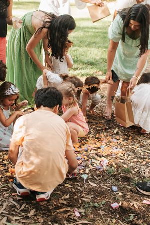 Group of people in green and white dresses gathering around scattered items on mulch at an outdoor party.