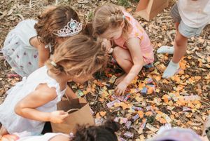 Small children in party attire searching through scattered items on ground at outdoor gathering.