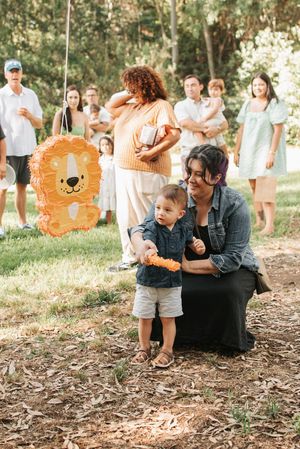 An outdoor family gathering with an orange lion piñata and spectators in the background.