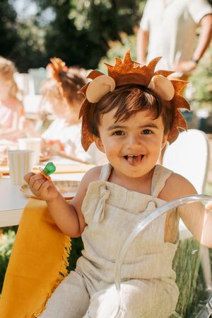 Toddler in white overalls and autumn leaf crown plays during an outdoor photoshoot.