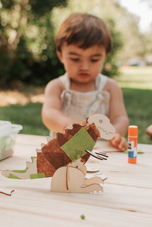 A brown paper dinosaur craft project sits on a wooden table outdoors.