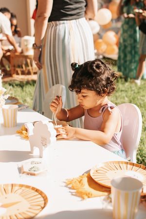 Child sitting at decorated party table with orange and gold themed place settings.