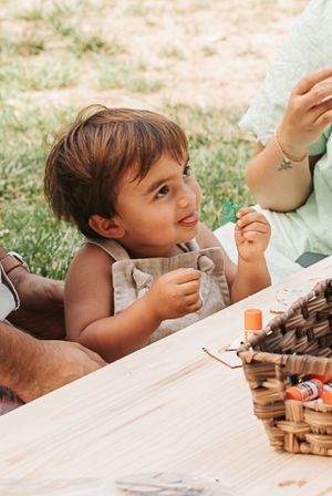 A small child sitting at a wooden table with craft supplies during an outdoor activity.