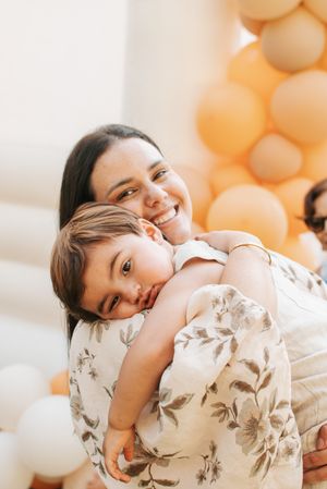 Sweet moment captured of parent and child hugging with peach balloons in background.