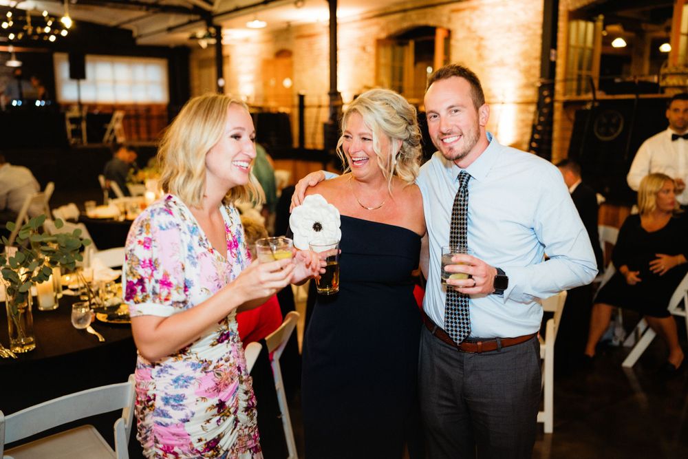 Wedding guests enjoying drinks and laughter during reception at rustic brick venue.